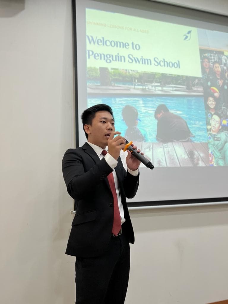 Remus Teo presenting Penguin Swim School with a microphone in a formal setting